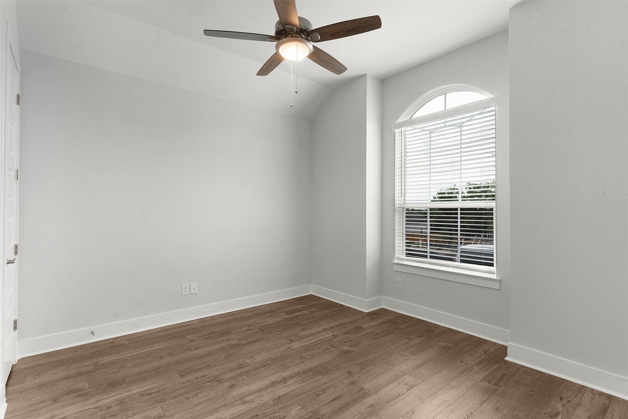 1129 Pansy Trail Georgetown, TX 78628 - Photo 5 of 29 Spacious room featuring a large arched window with blinds, a ceiling fan with light, wood-finish flooring, and white baseboards