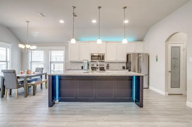 a kitchen with stainless steel appliances granite countertop a refrigerator a sink dishwasher a stove and white cabinets with wooden floor