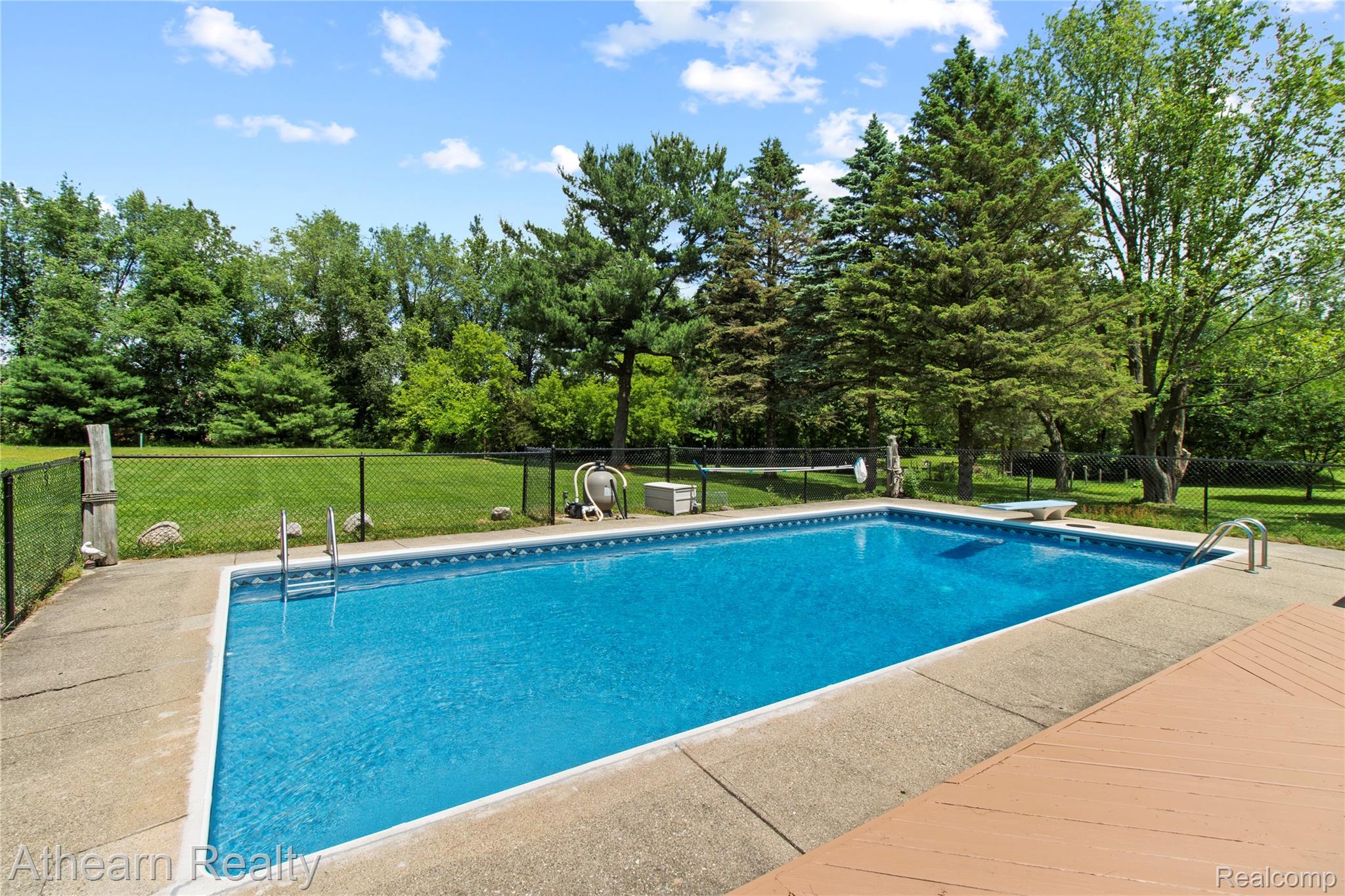 12427 Foley Road Fenton, MI 48430 - Photo 9 of 47 Rectangular swimming pool with a concrete surround, enclosed by a black chain-link fence
