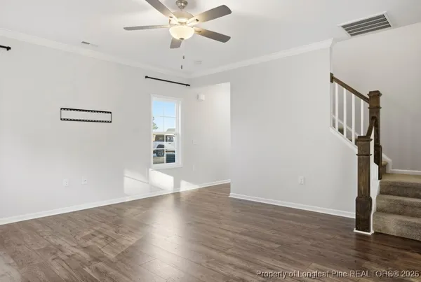 a view of an empty room with wooden floor and a ceiling fan