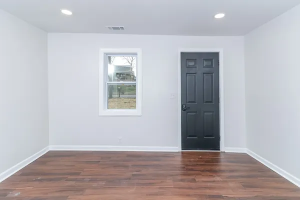 a view of an empty room with wooden floor and a window