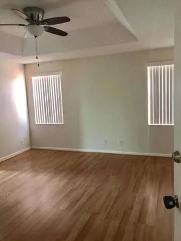 an empty room with wooden floor fan and windows