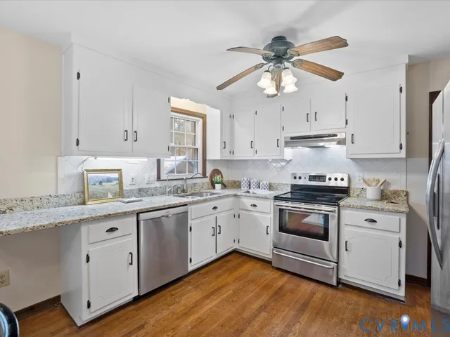 a kitchen with stainless steel appliances granite countertop a sink a stove a refrigerator and island with wooden floor