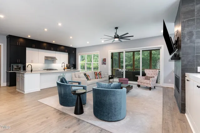 a living room with couches chairs kitchen view and a large window