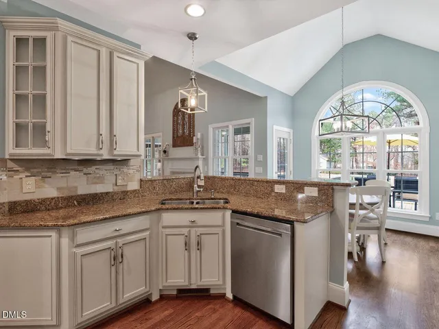 a open kitchen with granite countertop a stove a sink and white cabinets with wooden floor next to windows