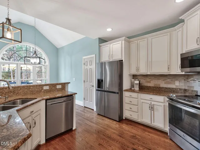 a kitchen with stainless steel appliances granite countertop a refrigerator a stove a sink and white cabinets with wooden floor