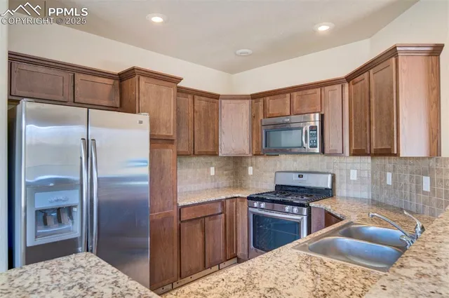 a kitchen with stainless steel appliances granite countertop a refrigerator a stove and a sink with wooden cabinets