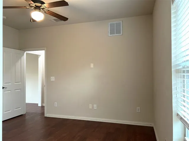 an empty room with wooden floor fan and windows
