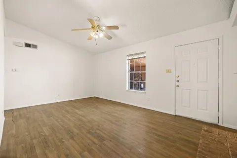 an empty room with wooden floor chandelier fan and windows