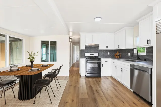 a kitchen with stainless steel appliances kitchen island granite countertop a stove top oven a sink a refrigerator with white cabinets and wooden floor