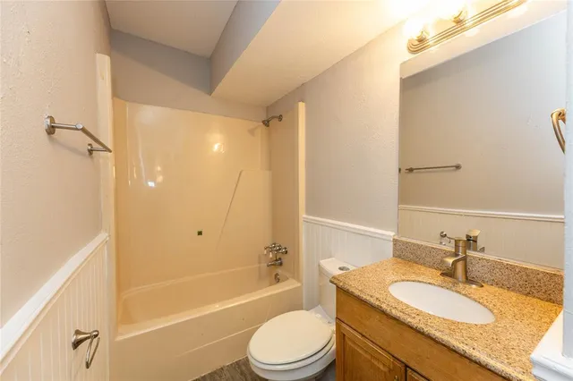 a bathroom with a granite countertop bathtub shower sink vanity mirror and toilet
