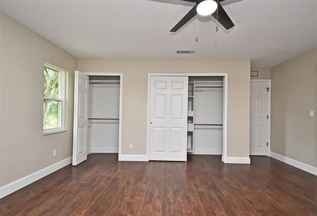 an empty room with wooden floor fan and windows