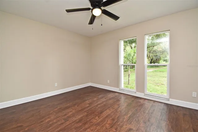 an empty room with wooden floor ceiling fan and windows