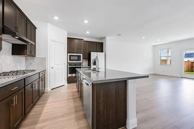 a kitchen with stainless steel appliances granite countertop a stove top oven a sink dishwasher and a refrigerator with wooden floor