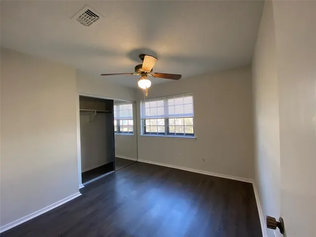 an empty room with wooden floor chandelier fan and windows