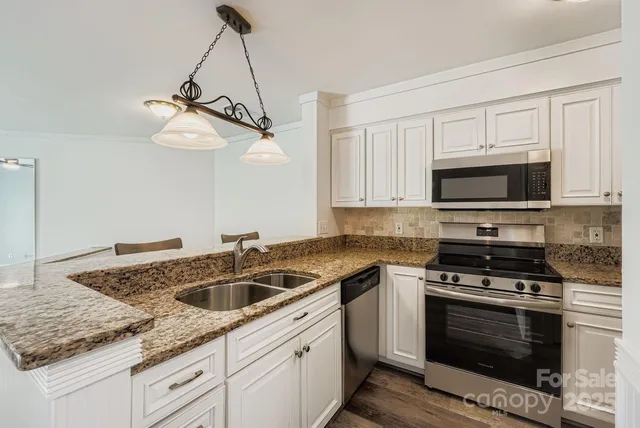 a kitchen with granite countertop a sink stainless steel appliances and white cabinets