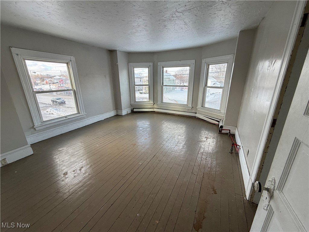 1020 West Prospect Road Ashtabula, OH 44004 - Photo 16 of 22 Empty room featuring a textured ceiling, a baseboard radiator, and wood-type flooring