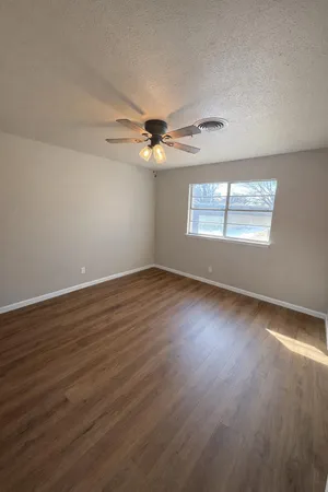 an empty room with wooden floor chandelier fan and windows