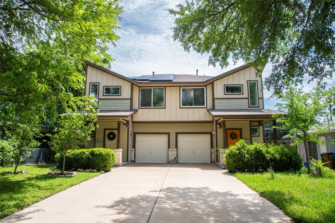 View of front facade featuring solar panels, board and batten siding, concrete driveway, and stone siding