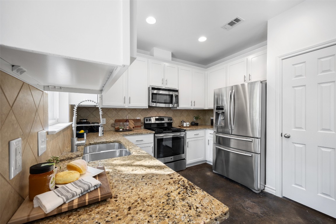 3407 Banton Road, Unit A Austin, TX 78722 - Photo 29 of 39 Kitchen with appliances with stainless steel finishes, concrete flooring, tasteful backsplash, white cabinetry, and light stone counters