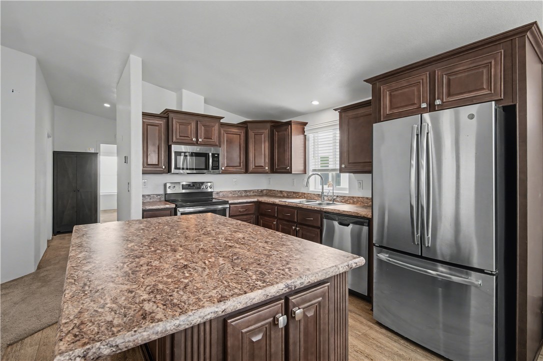 3058 West Carmichael Road Golden Valley, AZ 86413 - Photo 6 of 36 Kitchen featuring dark brown cabinetry, appliances with stainless steel finishes, a kitchen island, vaulted ceiling, and light wood-style flooring
