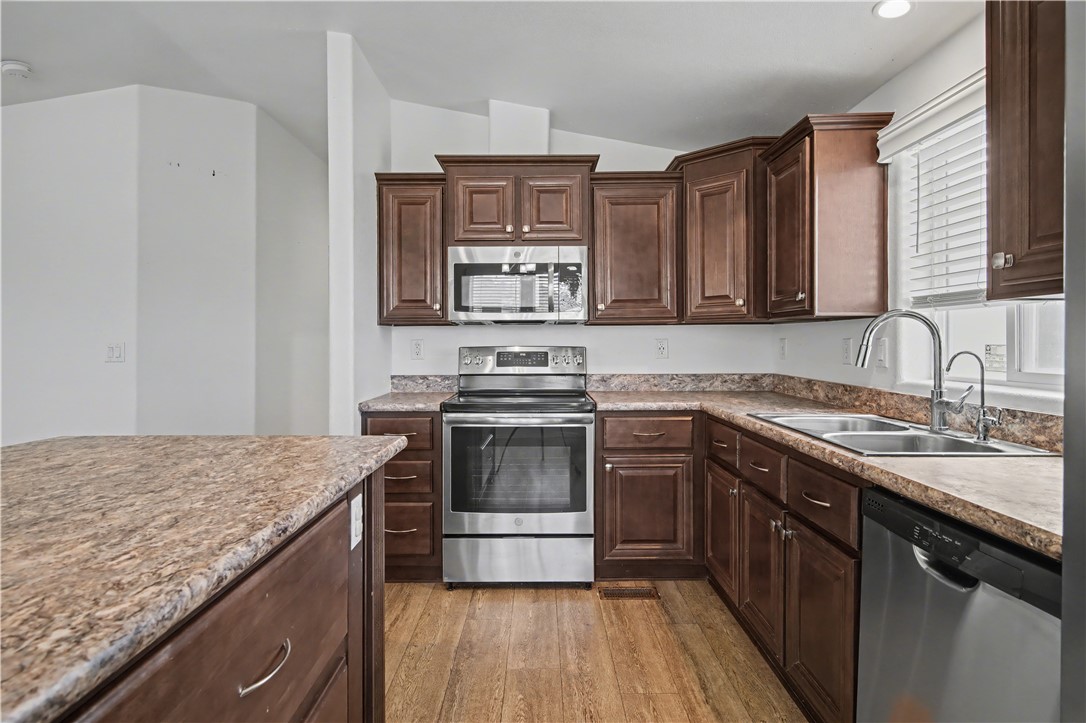 3058 West Carmichael Road Golden Valley, AZ 86413 - Photo 7 of 36 Kitchen featuring stainless steel appliances, dark brown cabinets, light wood-type flooring, light countertops, and vaulted ceiling