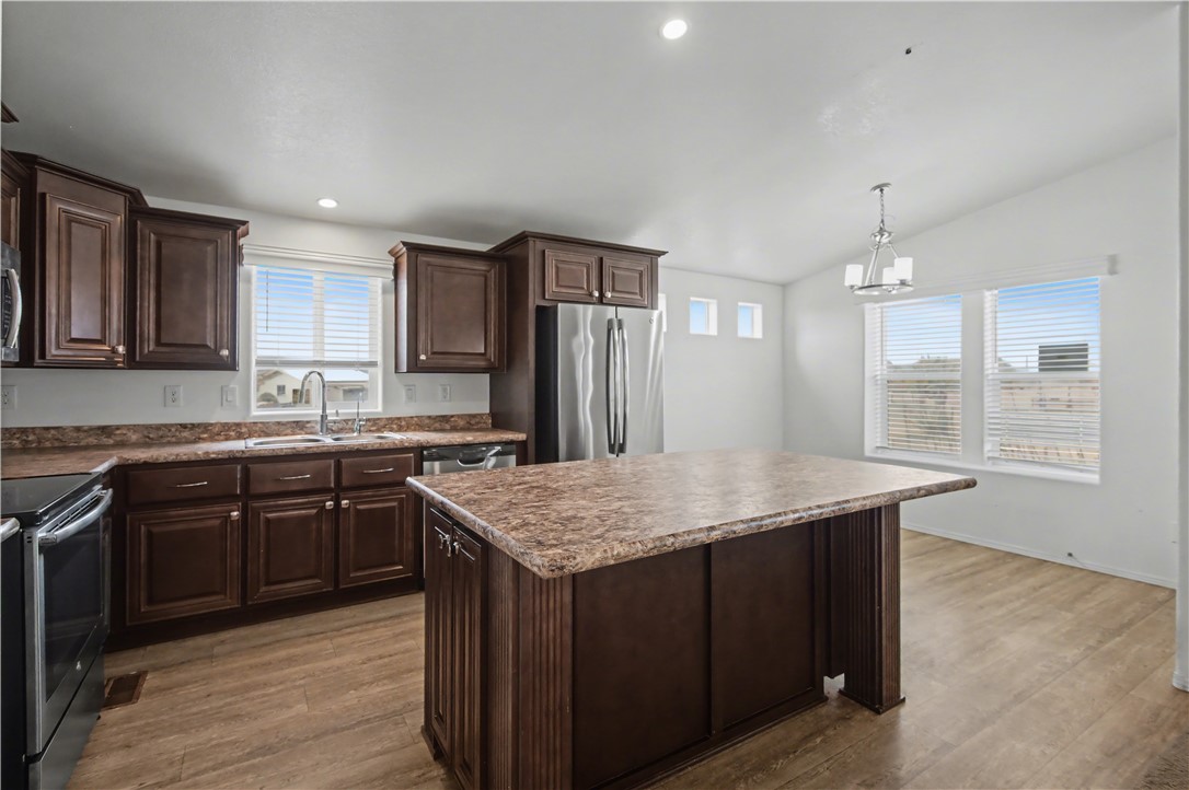 3058 West Carmichael Road Golden Valley, AZ 86413 - Photo 8 of 36 Kitchen with dark brown cabinetry, a kitchen island, appliances with stainless steel finishes, hanging light fixtures, and dark wood-style floors