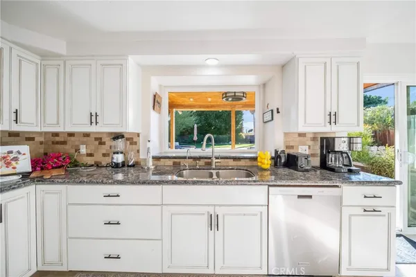 a kitchen with stainless steel appliances granite countertop a refrigerator a sink dishwasher a stove and white cabinets with wooden floor