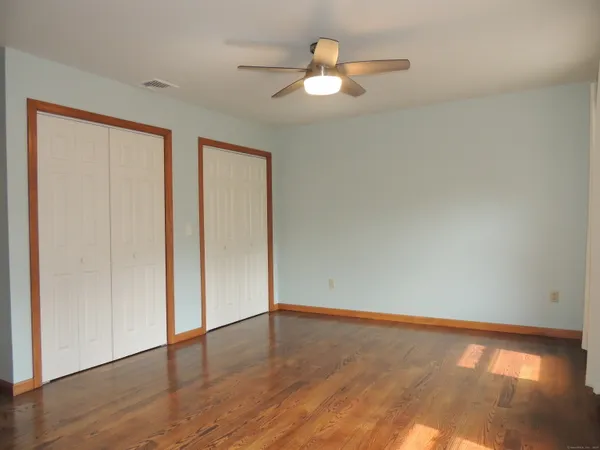 an empty room with wooden floor chandelier fan and windows