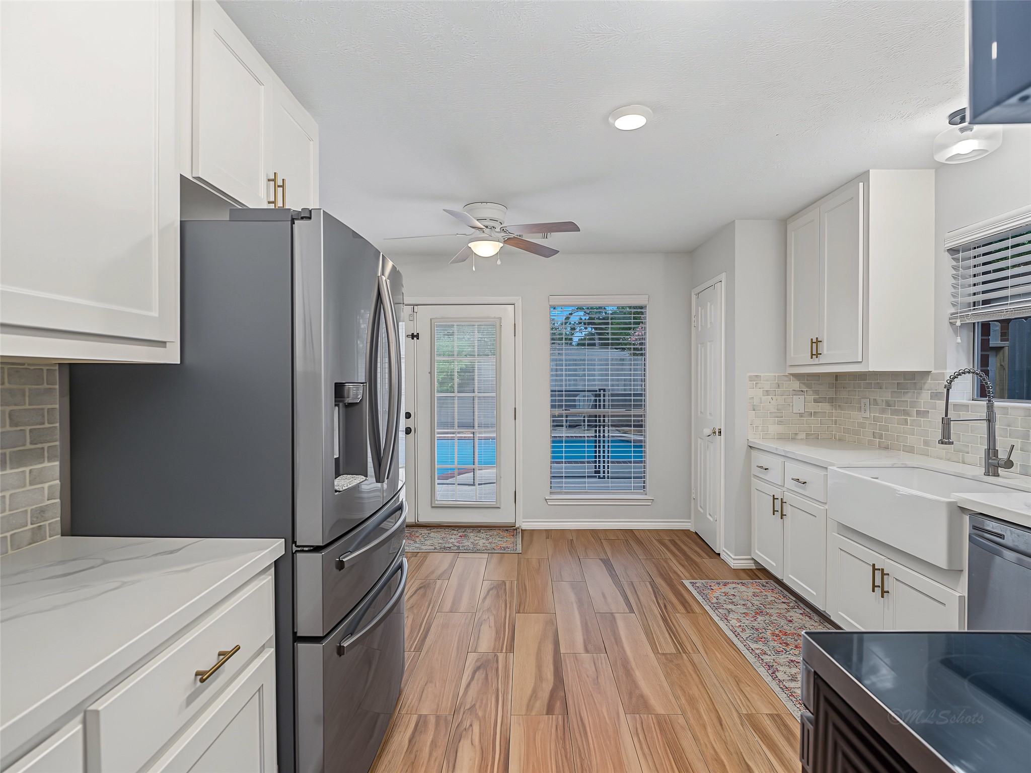 1310 Hidden Canyon Road Katy, TX 77450 - Photo 10 of 40 Bright and modern kitchen with sleek appliances, elegant white cabinetry, and a stylish farmhouse sink. Rich Tile flooring leads to a view of the inviting backyard pool through French doors, perfect for entertaining.