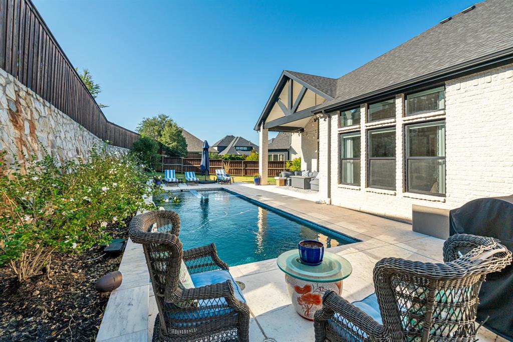8408 Twistpine Road Frisco, TX 75035 - Photo 27 of 38 Private backyard featuring a pool with water features, stone retaining wall, mature landscaping, and a covered patio