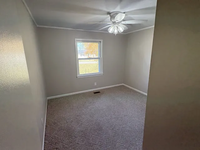 an empty room with a chandelier fan and windows