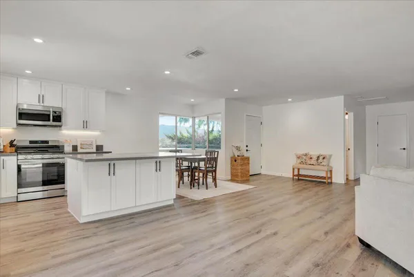 a kitchen with granite countertop a stove top oven a sink a dining table and chairs with wooden floor