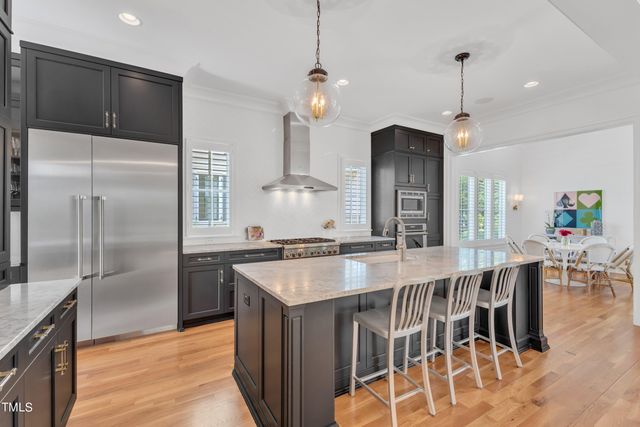 a kitchen with stainless steel appliances granite countertop a kitchen island a stove a refrigerator a sink a dining table and chairs with wooden floor