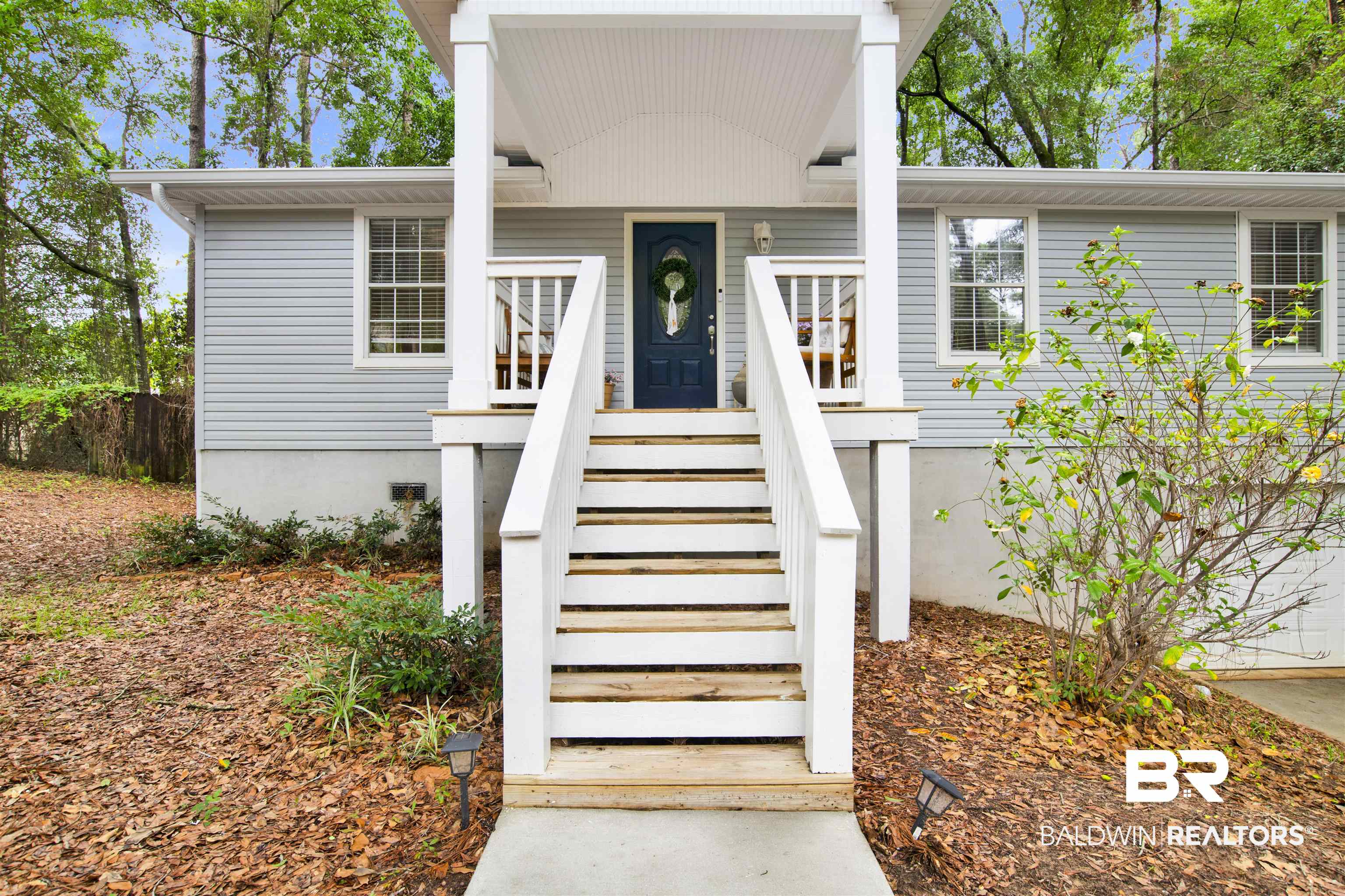 253 Maplewood Loop Daphne, AL 36526 - Photo 29 of 30 Light blue siding exterior featuring a covered front porch with white railings, a dark blue front door with an oval glass insert, and a concrete pathway leading to the entry