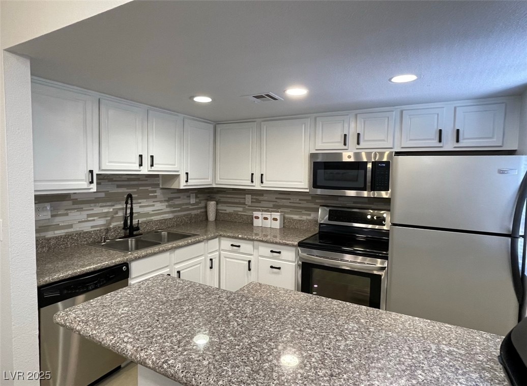 Kitchen with stainless steel appliances, recessed lighting, white cabinetry, decorative backsplash, and dark stone counters