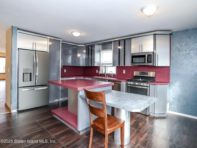 a kitchen with stainless steel appliances kitchen island granite countertop a refrigerator a stove a microwave oven a dining table and chairs with wooden floor