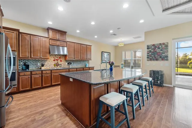 a kitchen with stainless steel appliances granite countertop a stove top oven a sink dishwasher a dining table and chairs with wooden floor