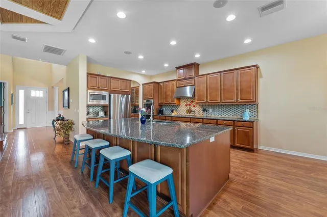 a kitchen with stainless steel appliances granite countertop a refrigerator a stove top oven and a dining table with wooden floor