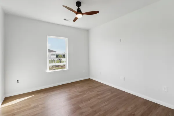 an empty room with wooden floor ceiling fan and window