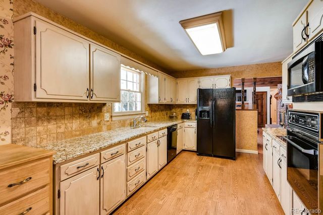 a kitchen with stainless steel appliances granite countertop a refrigerator a sink dishwasher a stove and white cabinets with wooden floor