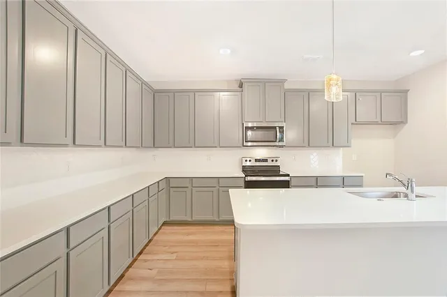 a kitchen with stainless steel appliances a sink dishwasher a stove top oven a refrigerator with white cabinets and wooden floor