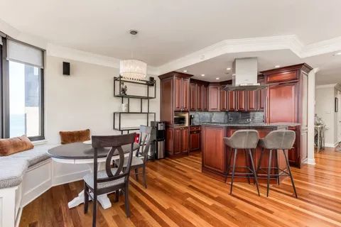 a kitchen with stainless steel appliances kitchen island granite countertop a dining table chairs and a refrigerator