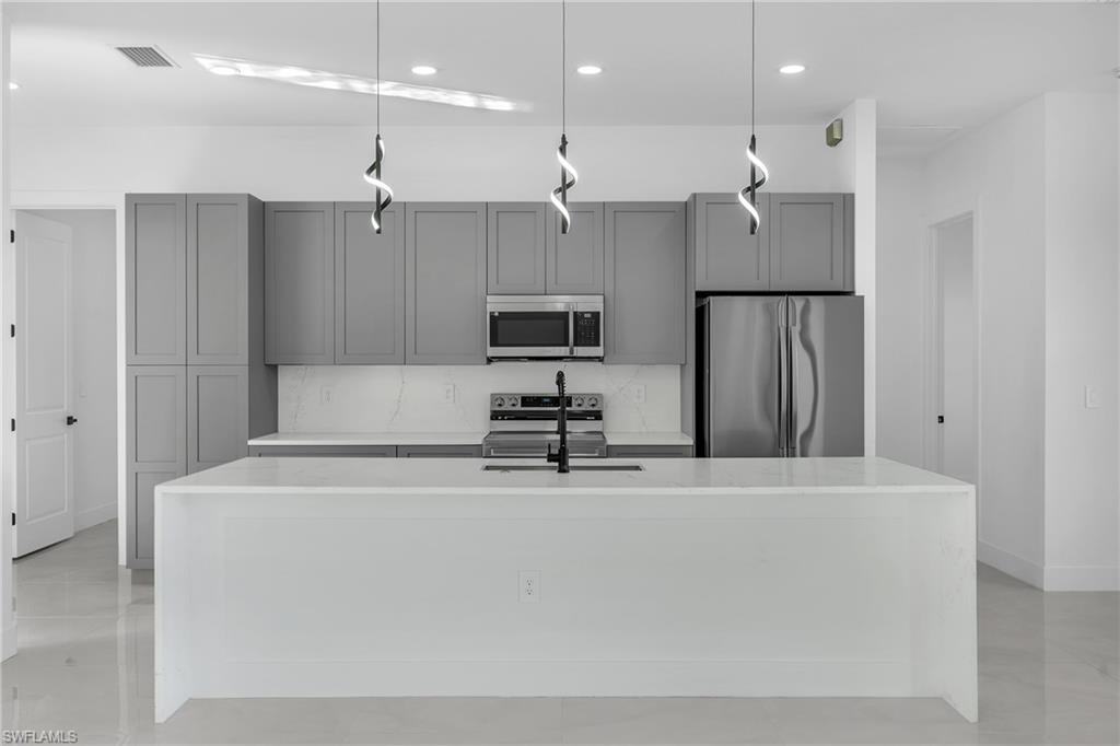 3110 23rd Street Southwest Lehigh Acres, FL 33976 - Photo 3 of 16 Kitchen with light stone counters, appliances with stainless steel finishes, tasteful backsplash, a center island with sink, and gray cabinets