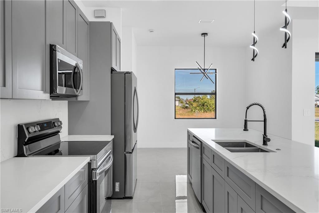 3110 23rd Street Southwest Lehigh Acres, FL 33976 - Photo 4 of 16 Kitchen featuring gray cabinetry, appliances with stainless steel finishes, light stone counters, decorative light fixtures, and a chandelier