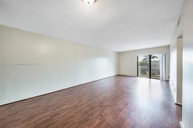 a view of an empty room with wooden floor and windows