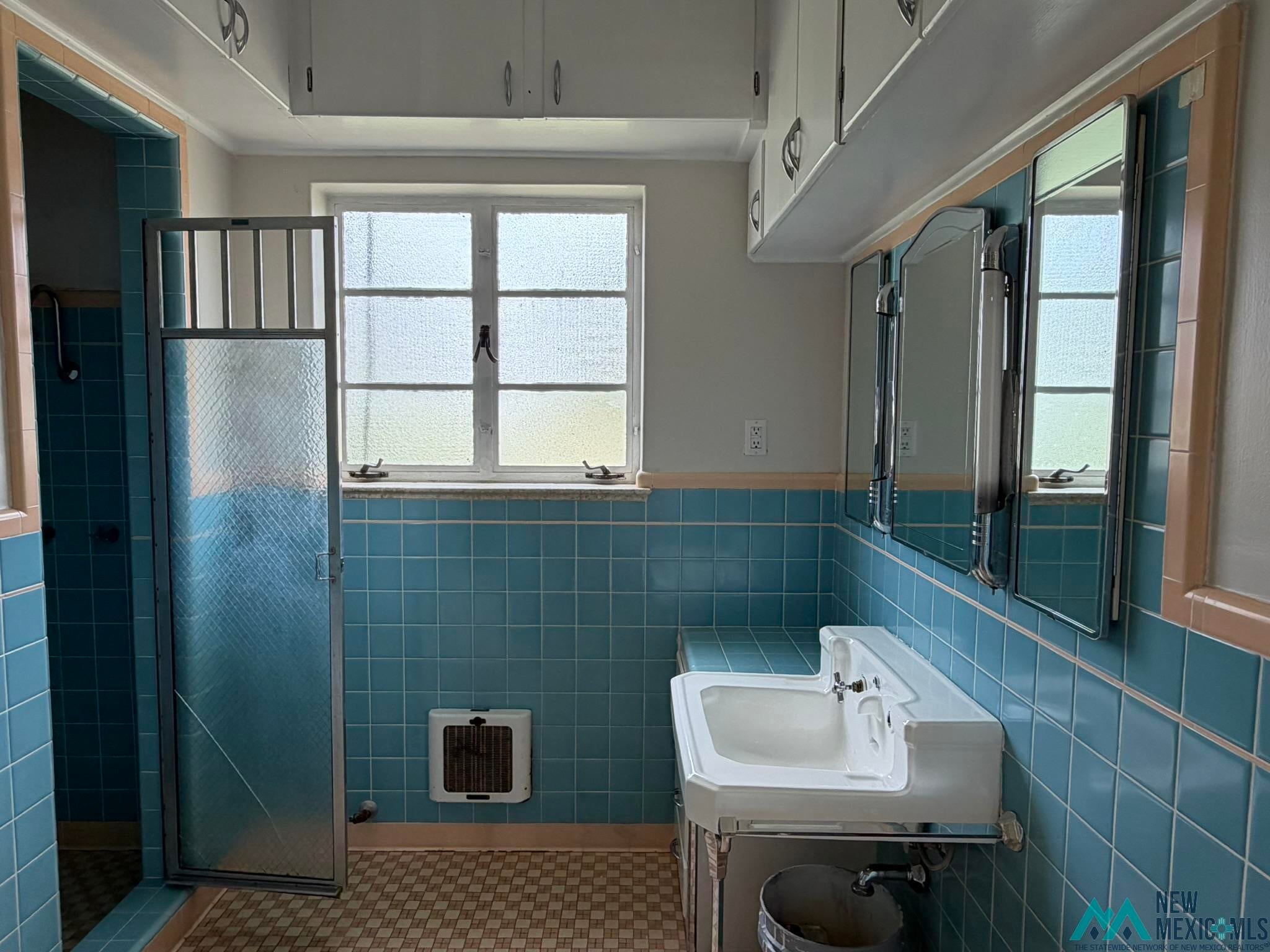 570 Curry Road North Clovis, NM 88101 - Photo 32 of 59 Bathroom featuring blue tiled walls with a contrasting trim, a white pedestal sink, multiple medicine cabinets with integrated lighting, and a shower with a translucent glass door