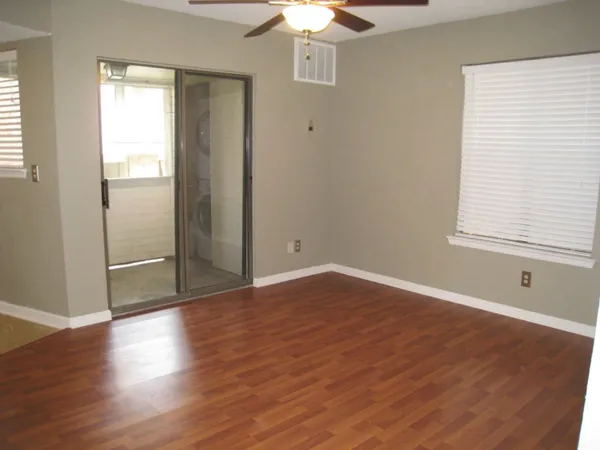 a view of a livingroom with wooden floor a ceiling fan and windows