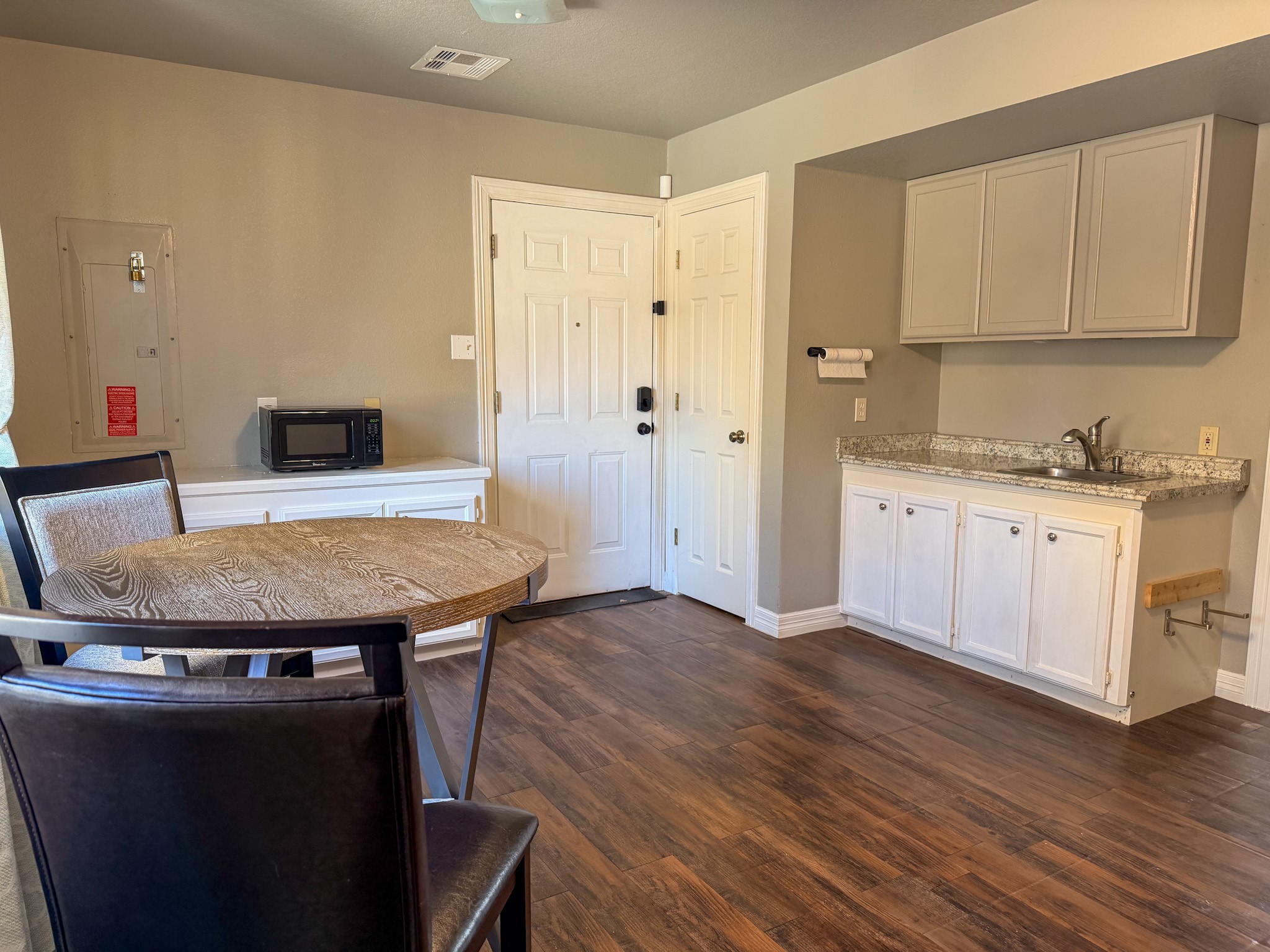24527 Appian Ridge, Unit B Porter, TX 77365 - Photo 3 of 10 This cozy space features a small dining area with a round table and chairs, a kitchenette with cabinets and a granite countertop, and wood flooring. Ideal for a compact living setup.