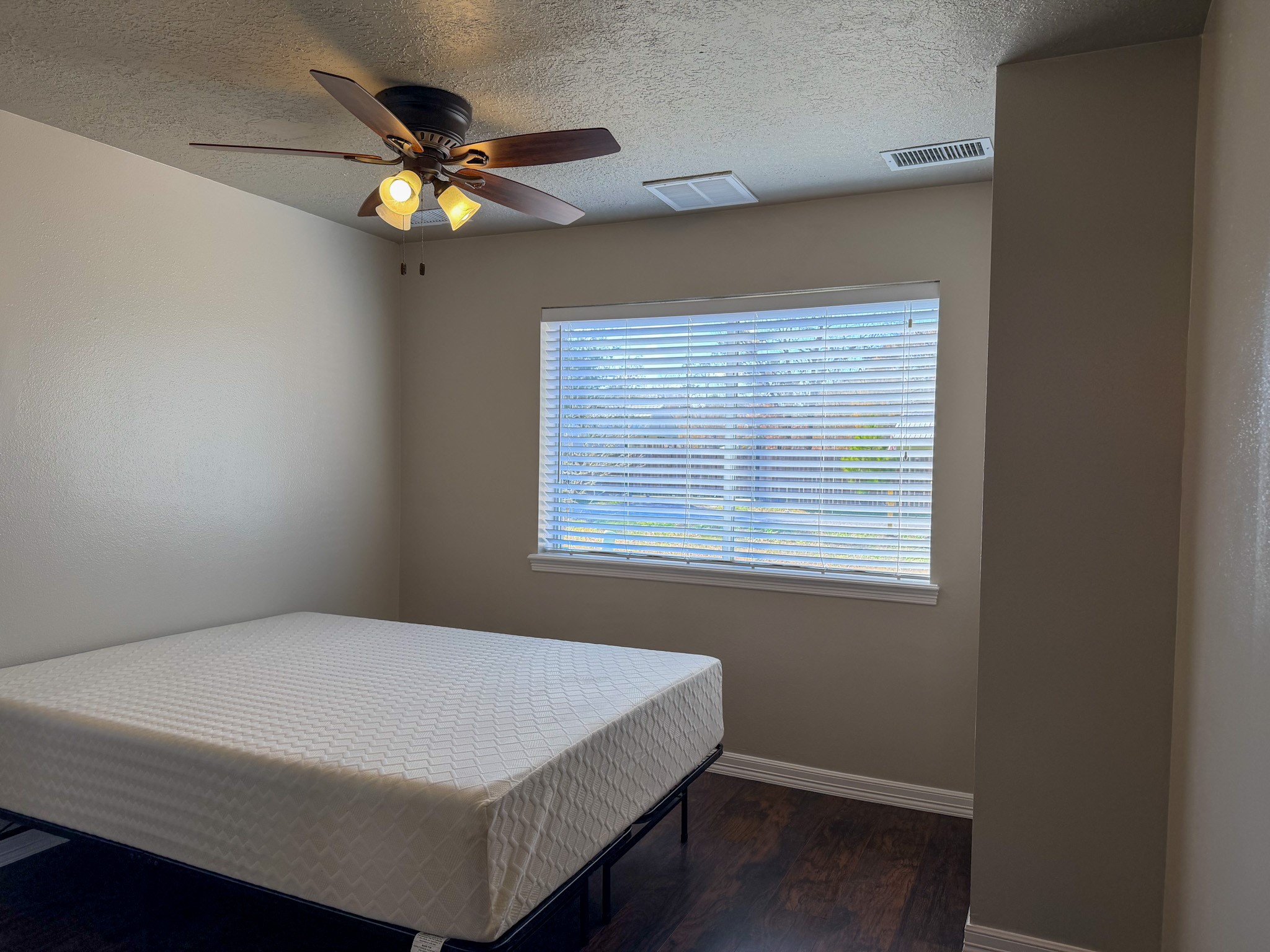 24527 Appian Ridge, Unit B Porter, TX 77365 - Photo 6 of 10 This is a cozy bedroom featuring a ceiling fan and a large window with blinds, allowing for natural light. The room has neutral walls and dark hardwood floors, creating a warm ambiance.
